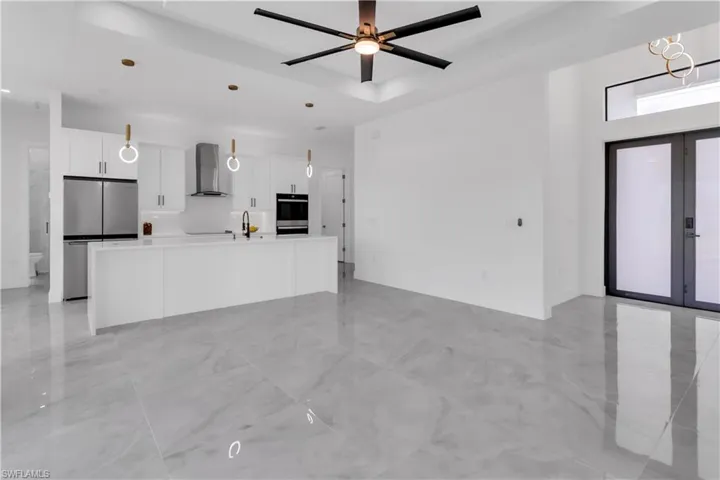 Kitchen with decorative light fixtures, stainless steel appliances, wall chimney exhaust hood, ceiling fan, and a kitchen island with sink