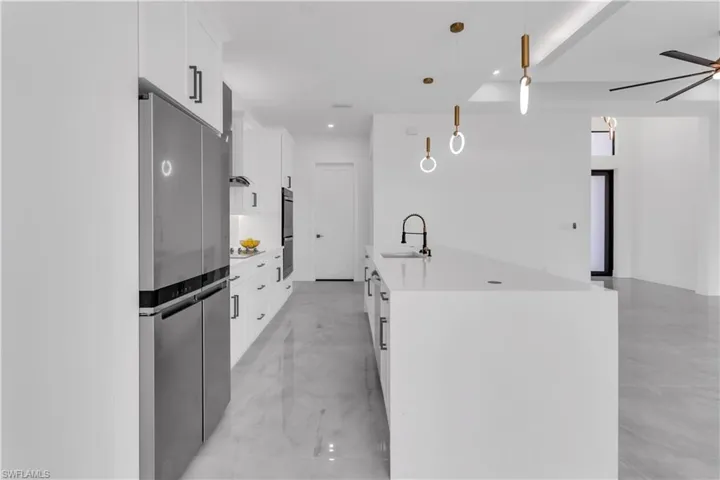 Kitchen featuring pendant lighting, stainless steel appliances, sink, ceiling fan, and white cabinets