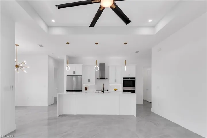 Kitchen featuring wall chimney exhaust hood, appliances with stainless steel finishes, an island with sink, and hanging light fixtures