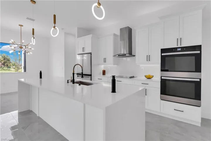 Kitchen with wall chimney exhaust hood, stainless steel double oven, decorative light fixtures, and white refrigerator