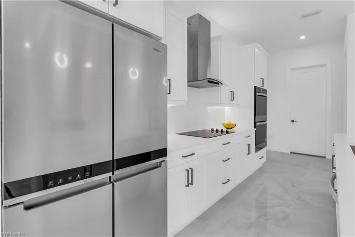 Kitchen with wall chimney range hood, appliances with stainless steel finishes, and white cabinets