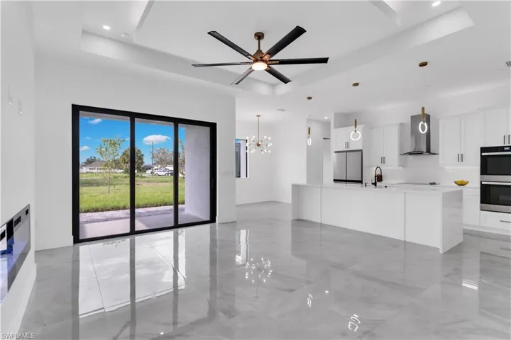 Unfurnished living room featuring ceiling fan with notable chandelier, a raised ceiling, and sink