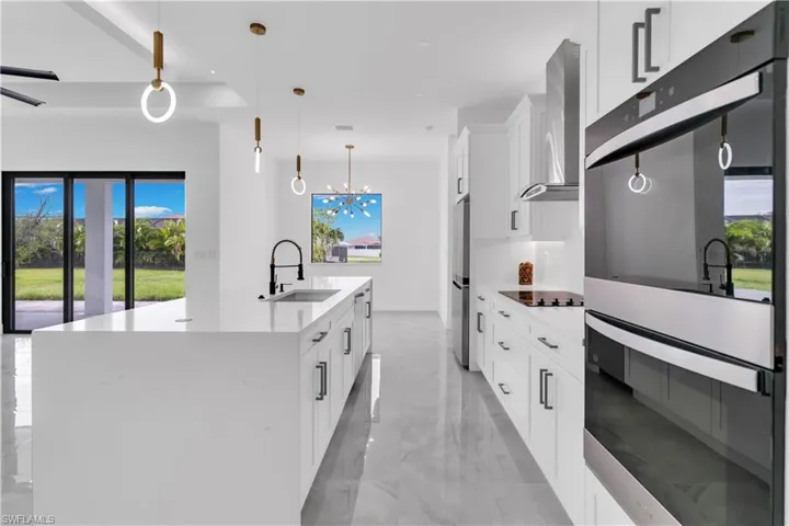 Kitchen featuring wall chimney range hood, hanging light fixtures, plenty of natural light, and sink
