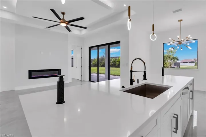 Kitchen with a kitchen island with sink, ceiling fan with notable chandelier, white cabinetry, decorative light fixtures, and sink
