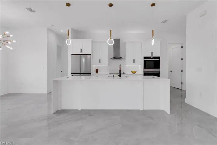Kitchen with an island with sink, appliances with stainless steel finishes, white cabinets, and wall chimney exhaust hood