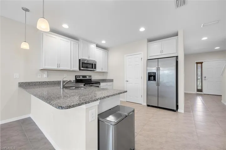 Kitchen with stainless steel appliances, decorative light fixtures, white cabinetry, and light tile floors