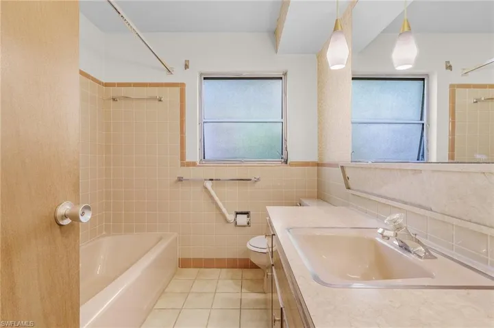 Full bathroom servicing the guest bedrooms with vanity, toilet, tiled shower / bath combo, tile walls, and tile patterned flooring