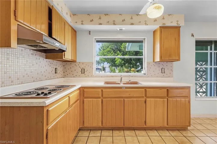 Kitchen featuring tasteful backsplash, light tile patterned flooring, sink, white electric stovetop, and light brown cabinets
