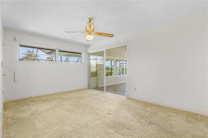 Carpeted primary bedroom featuring ceiling fan,sliders to the Florida room and pool, walk in closet and private bath