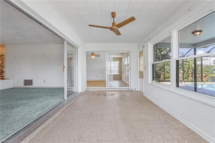 Unfurnished sunroom featuring ceiling fan, vinyl flooring, sliders to the primary bedroom and new windows with roll down hurricane shutters on all windows and door to lanai and pool