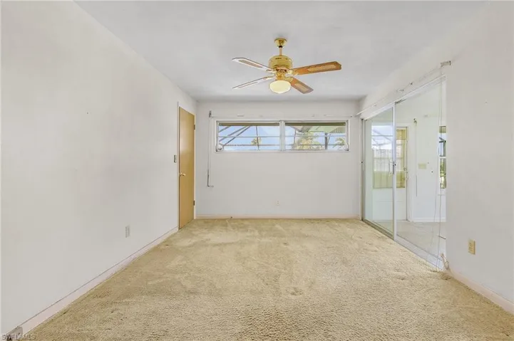 Carpeted primary bedroom with ceiling fan, sliders to the Florida room and pool, walk in closet and private bathroom