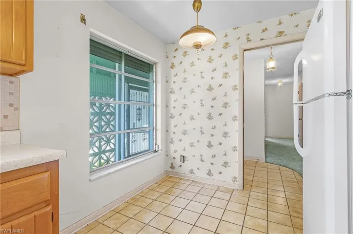 Kitchen with white refrigerator, decorative light fixtures, and light tile patterned floors and breakfast nook. Lots of cabinets and pantry in kitchen