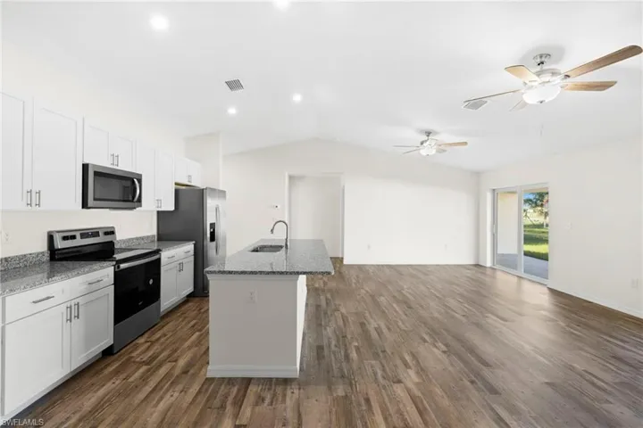 Kitchen with appliances with stainless steel finishes, white cabinetry, a kitchen island with sink, open floor plan, and dark stone counters