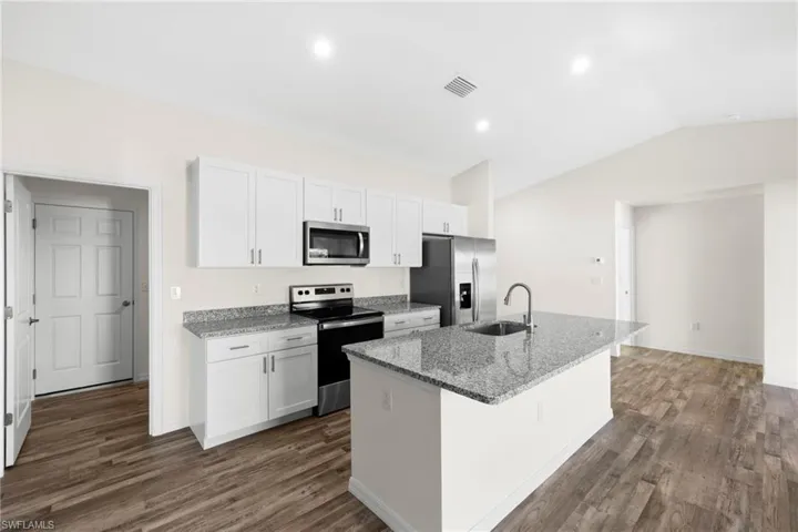 Kitchen featuring stainless steel appliances, light stone countertops, white cabinetry, a center island with sink, and dark wood finished floors