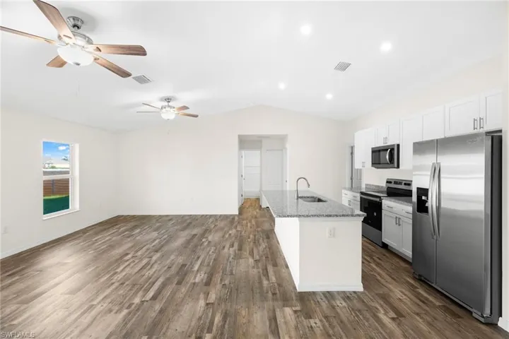 Kitchen featuring stainless steel appliances, a kitchen island with sink, open floor plan, white cabinets, and light stone countertops