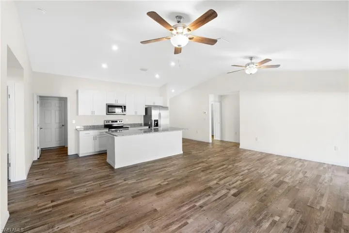 Kitchen featuring open floor plan, white cabinets, lofted ceiling, a kitchen island with sink, and dark wood-style floors