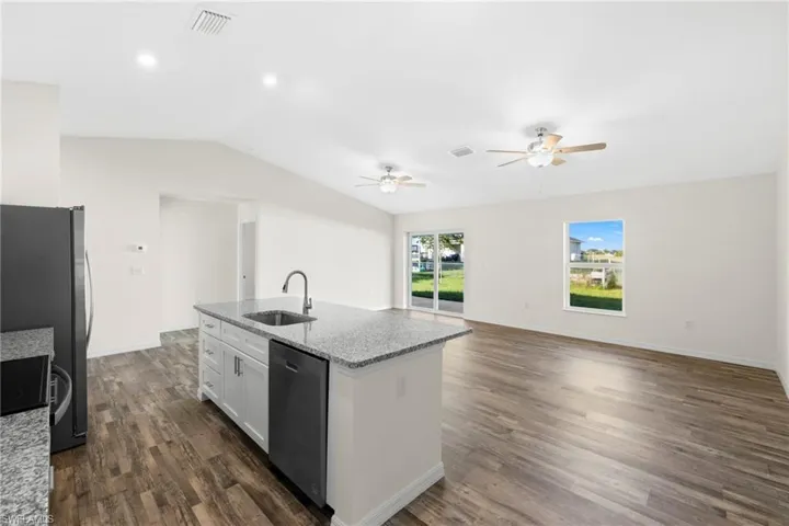 Kitchen with light stone countertops, open floor plan, a kitchen island with sink, stainless steel appliances, and white cabinetry