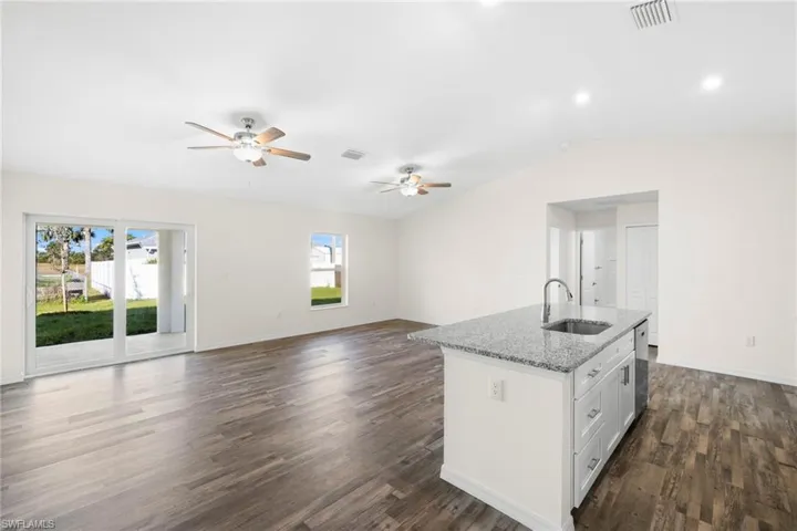 Kitchen featuring light stone countertops, white cabinetry, open floor plan, an island with sink, and dark wood-style flooring