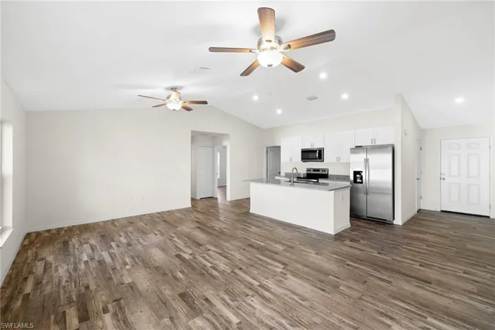 Kitchen featuring open floor plan, appliances with stainless steel finishes, vaulted ceiling, white cabinetry, and a kitchen island with sink