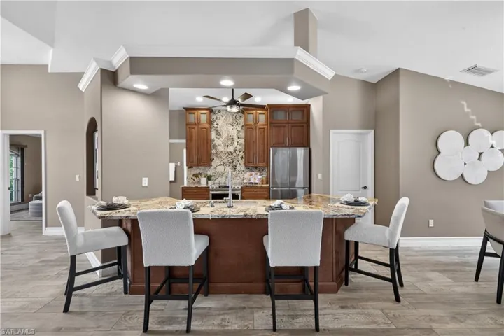 Kitchen with a breakfast bar area, wood finish cabinets, light stone countertops, light wood-style flooring, and recessed lighting