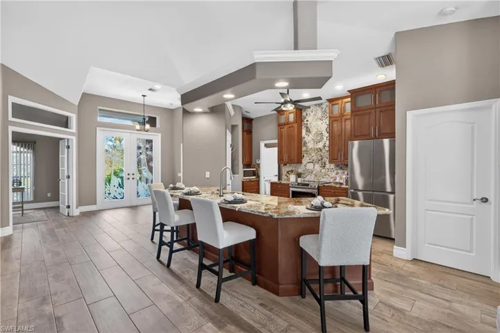 Kitchen with french doors, wood finish cabinetry, a breakfast bar area, light stone counters, and stainless steel appliances