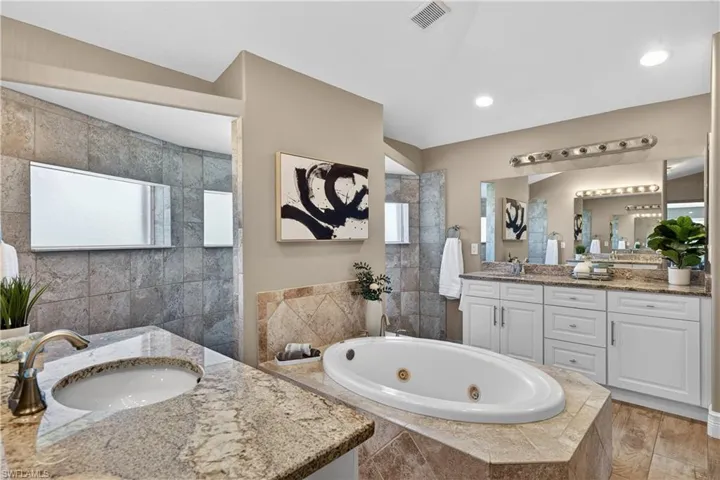 Full bathroom featuring two vanities, a tub with jets, and walk in shower