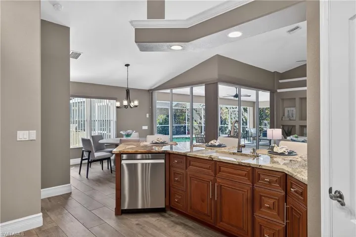 Kitchen with dishwasher, wood finish cabinetry, vaulted ceiling, wood finish floors, and light stone counters