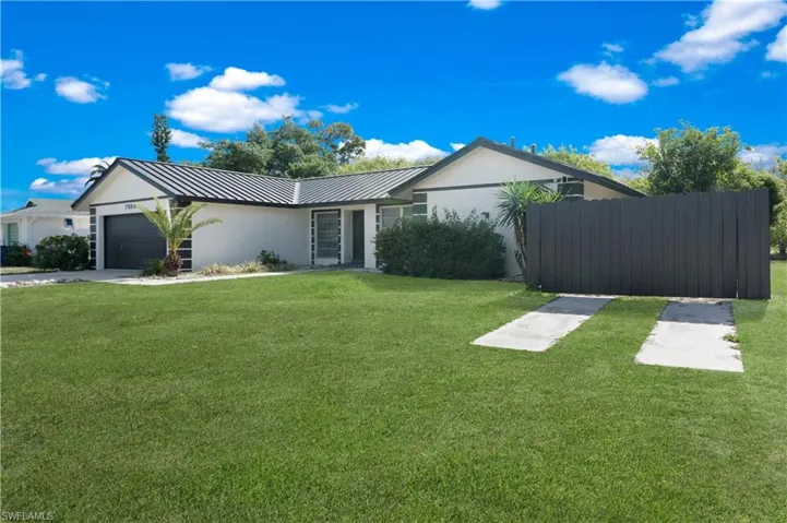 Ranch-style house featuring stucco siding, an attached garage, a standing seam roof, and driveway
