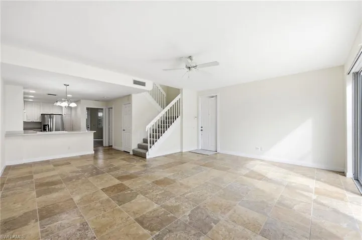 Unfurnished living room featuring ceiling fan, a chandelier, and stone tile floors