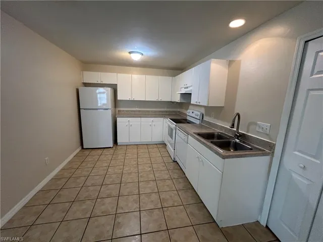 Kitchen with white appliances, light tile patterned flooring, white cabinets, dark countertops, and under cabinet range hood