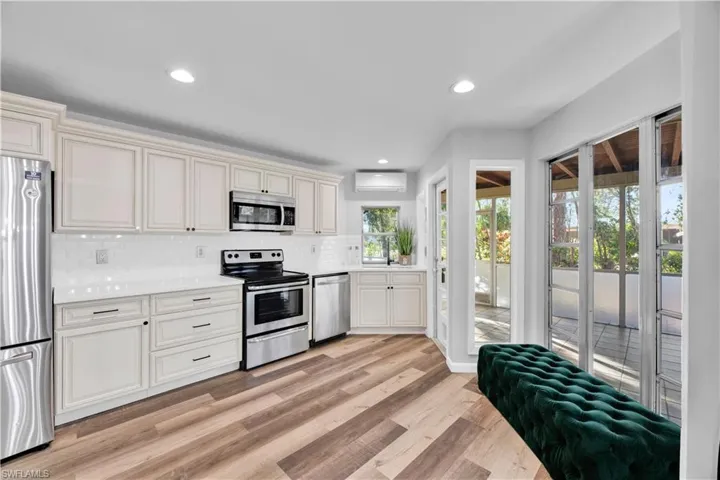 Kitchen featuring light countertops, a wall unit AC, decorative backsplash, light wood finished floors, and appliances with stainless steel finishes