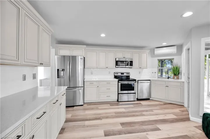 Kitchen with a wall unit AC, recessed lighting, stainless steel appliances, light wood finished floors, and backsplash