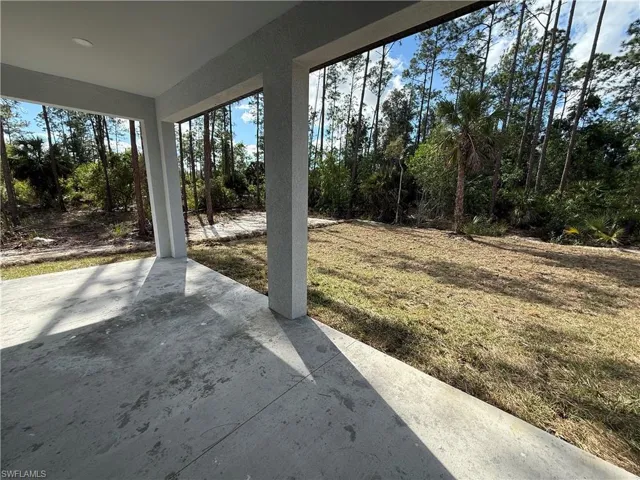 View of grassy yard with a patio and view of scattered trees