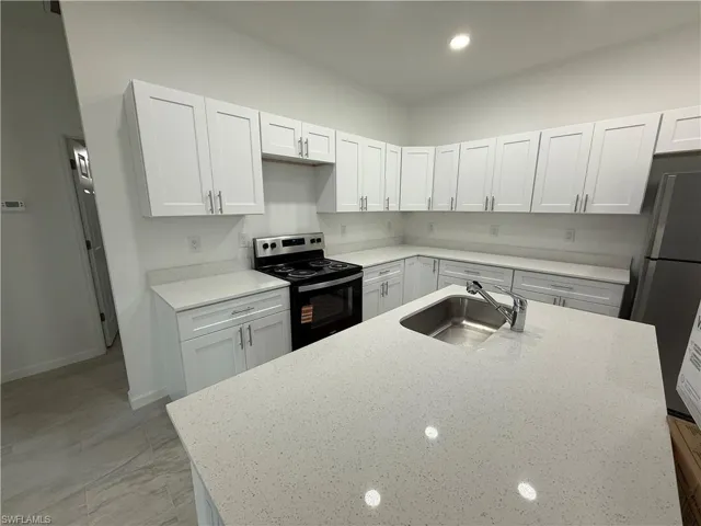 Kitchen featuring stainless steel appliances, white cabinets, light stone countertops, and a center island with sink