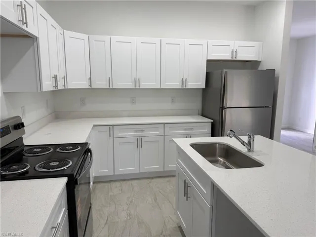 Kitchen featuring black electric range oven, freestanding refrigerator, light marble finish floors, light stone counters, and white cabinetry