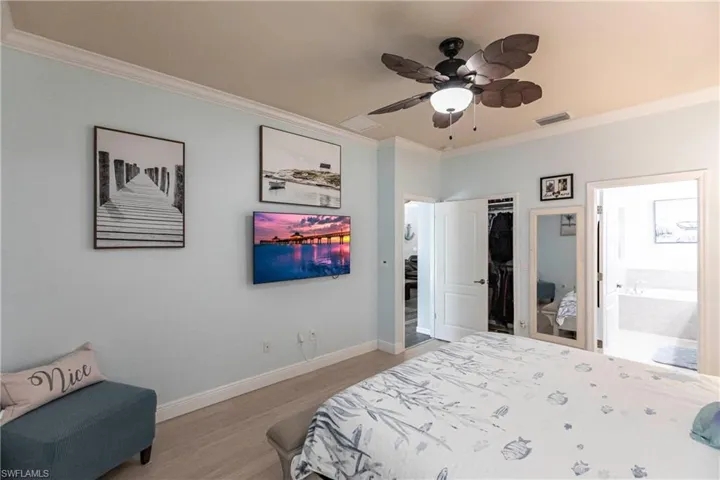 Bedroom featuring ceiling fan, a closet, crown molding, ensuite bath, and wood-type flooring