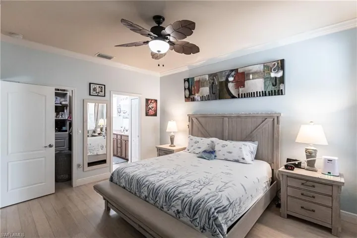 Bedroom with ensuite bathroom, ceiling fan, light wood-type flooring, and crown molding