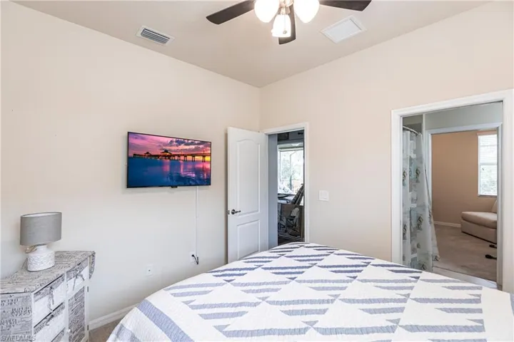 Bedroom featuring carpet flooring, ensuite bath, ceiling fan, and multiple windows