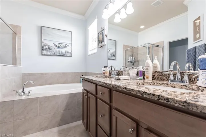 Bathroom with tile floors, crown molding, double vanity, and separate shower and tub