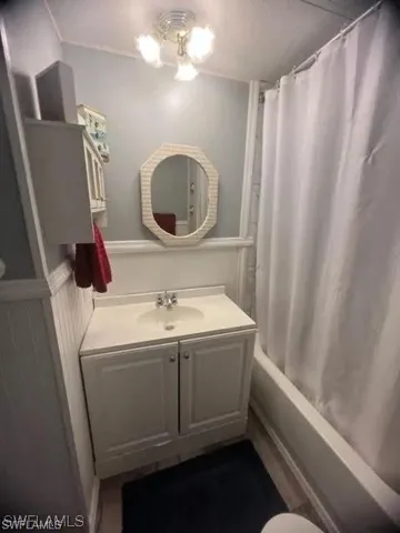 Bathroom featuring a white vanity with integrated sink, octagonal mirror, white wainscoting, and a full-size bathtub with shower