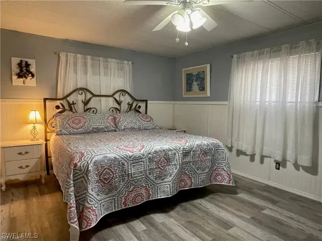 Bedroom featuring plank-style flooring, white wainscoting, and a ceiling fan with integrated lighting
