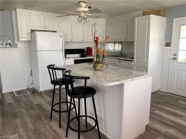 Kitchen featuring white cabinetry, a central island with a stone-finish countertop, wood-finish flooring, and beadboard paneling