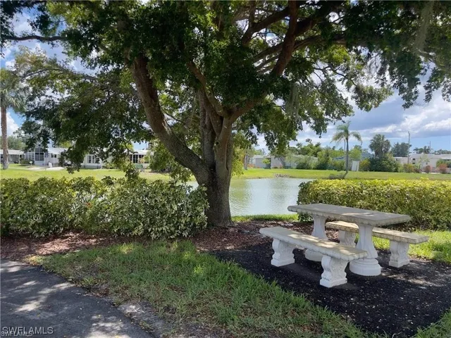 Tranquil outdoor area featuring a concrete picnic table and benches, mature tree, manicured lawn, and water feature