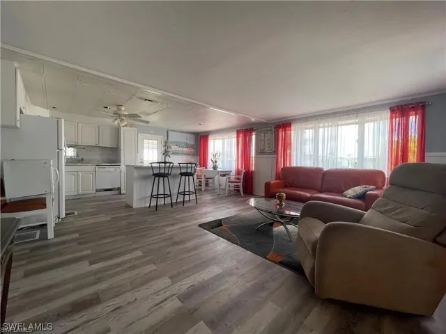 Open concept living space featuring wood-finish flooring, a kitchen island with seating, white cabinetry, and multiple windows