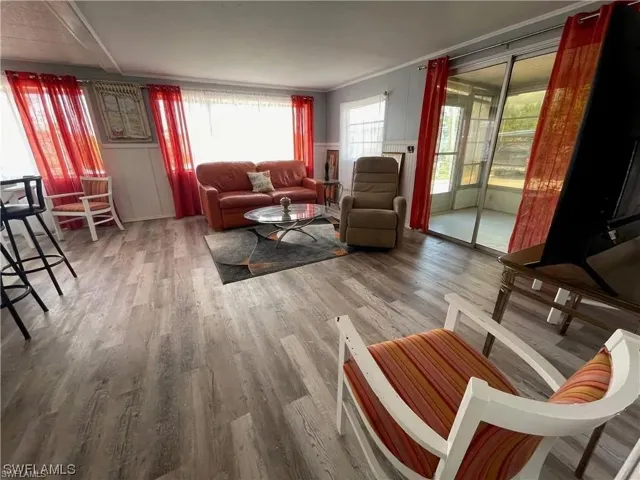 Living area featuring wood-finish flooring, white wainscoting, and large windows with privacy sheers