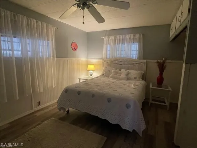 Bedroom featuring wood-finish flooring, beadboard wall paneling, and a ceiling fan with integrated lighting