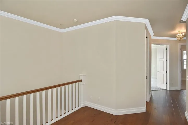 Hall featuring ornamental molding, dark wood-type flooring, and an inviting chandelier
