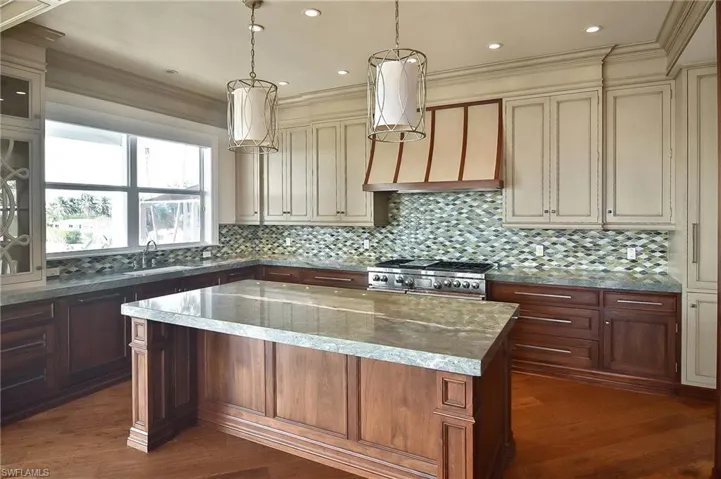 Kitchen with range, a center island, hanging light fixtures, light stone countertops, and cream cabinetry