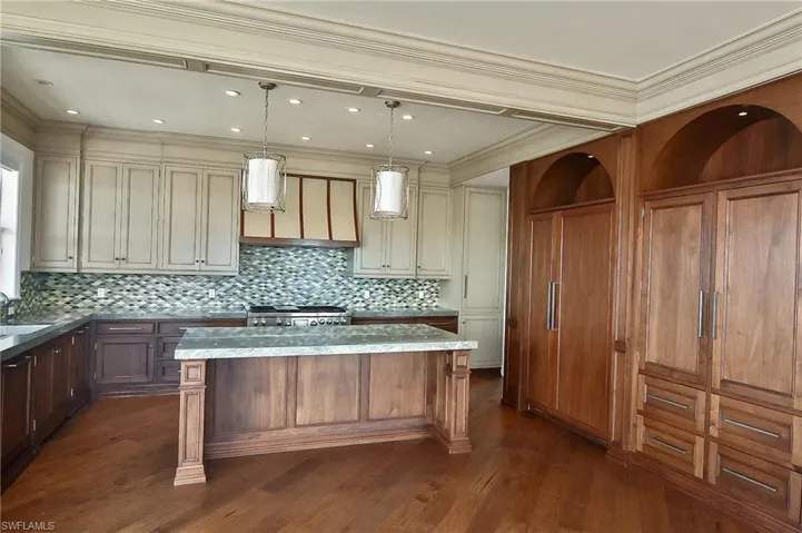 Kitchen with light stone counters, decorative light fixtures, a kitchen island, and cream cabinetry