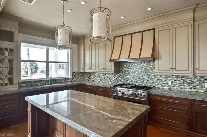 Kitchen featuring double oven range, light stone countertops, cream cabinets, and a kitchen island